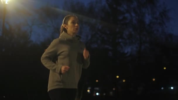 Corre por la noche. chica corre a lo largo del terraplén en el fondo de la ciudad nocturna. una joven deportista practicando al aire libre — Vídeo de stock