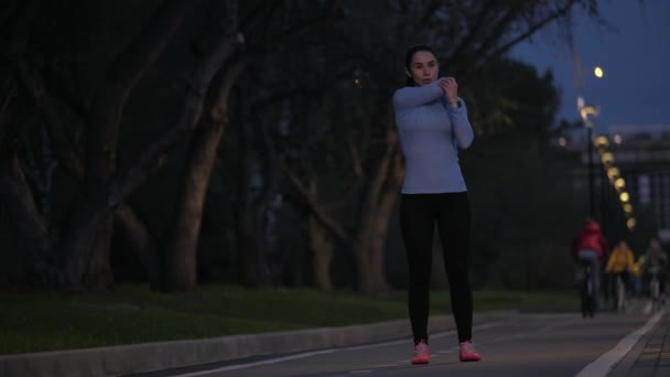 Σπορ κορίτσι κάνει διατάσεις πριν από την κατάρτιση στο πάρκο βράδυ. η αθλήτρια που προετοιμάζει για εκπαίδευση στην ύπαιθρο. — Αρχείο Βίντεο