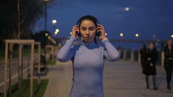 Дівчина одягає навушники і починає бігати по місту вночі. спортсмен поїзди на місячному світлі — стокове відео