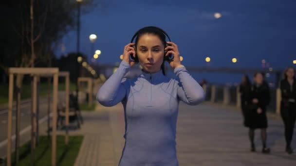 Ragazza si mette le cuffie e inizia a correre attraverso la città di notte. atleta si allena al chiaro di luna — Video Stock