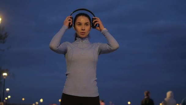 Κορίτσι βάζει ακουστικά και εγκαινιάζει μουσική σε ένα έξυπνο ρολόι και αρχίζει να τρέχει μέσα στην πόλη νύχτα. — Αρχείο Βίντεο