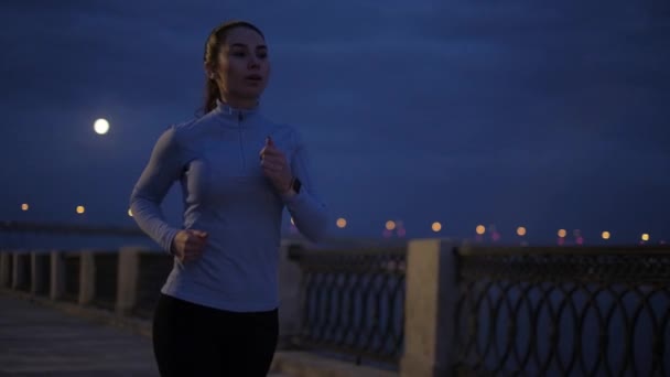 Correr à noite. jovem menina atraente em roupas esportivas Jogging na orla à noite. câmara lenta — Vídeo de Stock