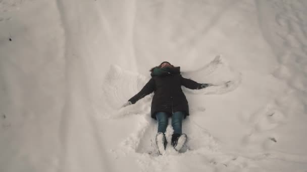 Chica hace un ángel de nieve en la nieve en el bosque — Vídeos de Stock