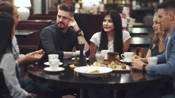 Vänner skratta och ha roligt sitter vid ett bord på en restaurang. Ett företag av vänner tillbringar tid tillsammans och tycker om umgänge. — Stockvideo