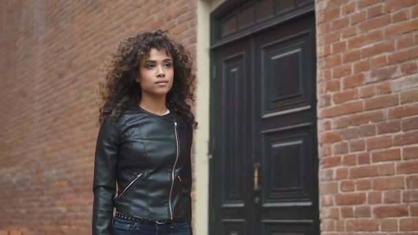 Portrait of a young stylish multi-ethnic girl. a girl in a black leather jacket walks down the street — Stock Video