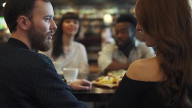 bir kafede bir masada arkadaş şirket. adam kız arkadaşına konuşuyor.