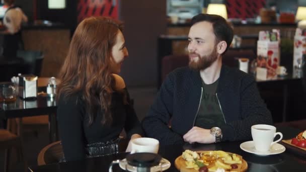 Pareja en una cita en un restaurante. chico y chica jóvenes se divierten hablando mientras están sentados en una mesa en un café o restaurante — Vídeos de Stock