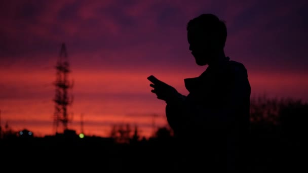 Silhouet van een jonge mannelijke toeristische bij zonsondergang. een man maakt gebruik van een mobiele telefoon — Stockvideo