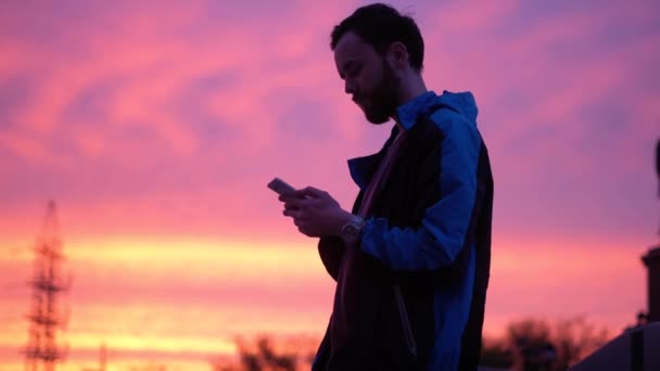 Silueta de un joven turista al atardecer. un hombre usa un teléfono móvil — Vídeo de stock