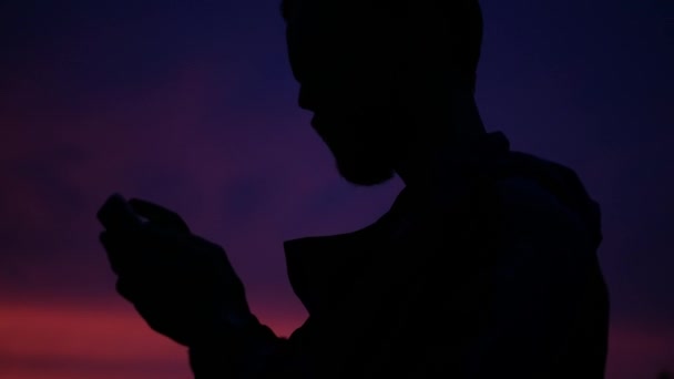 Silhouette di un giovane turista al tramonto. un uomo usa un telefono cellulare — Video Stock