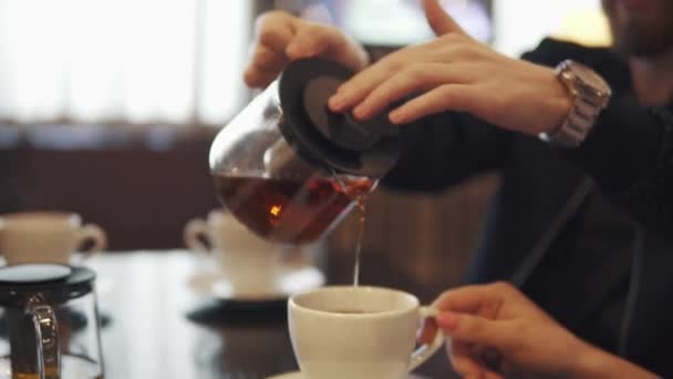 Een man giet thee uit een theepot in een mok — Stockvideo