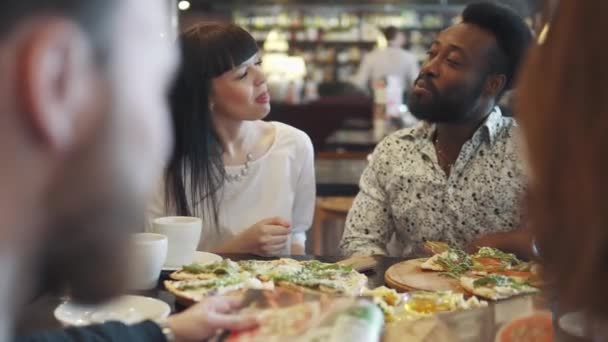 Багатоетнічна група друзів у кафе. молодий чорний чоловік і дівчина весело розмовляють і їдять — стокове відео