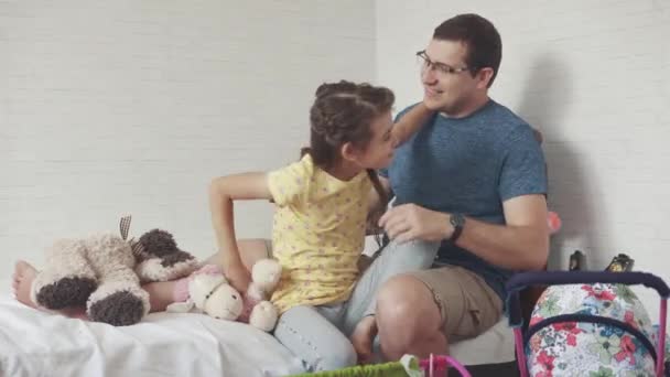 El joven padre y la hija juegan juntos en la habitación de los niños. la chica abraza a su padre — Vídeos de Stock