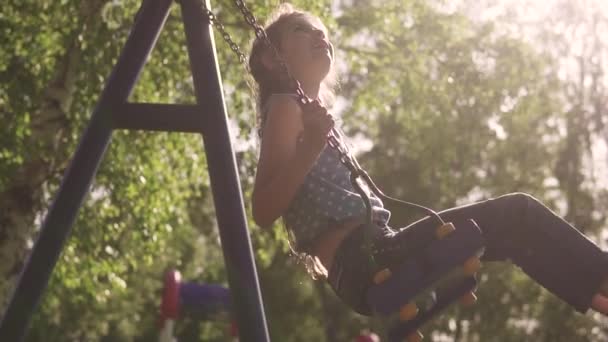 Child swings on a swing and laughs enthusiastically. little girl on a swing in the sunlight. concept of a happy and carefree childhood. slow motion — Stock Video