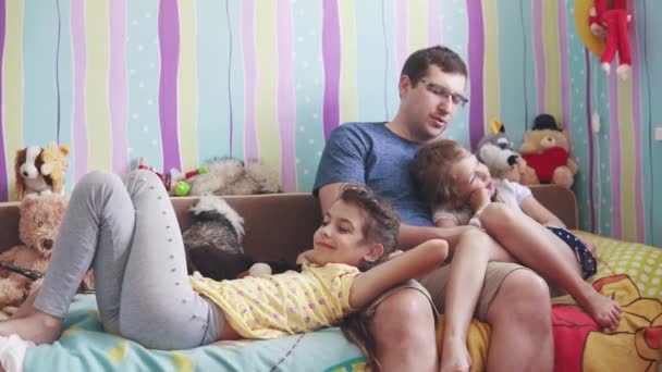 El padre joven y dos hijas pequeñas juegan con juguetes suaves, sonríen y ríen. padre disfruta del tiempo con los niños — Vídeos de Stock