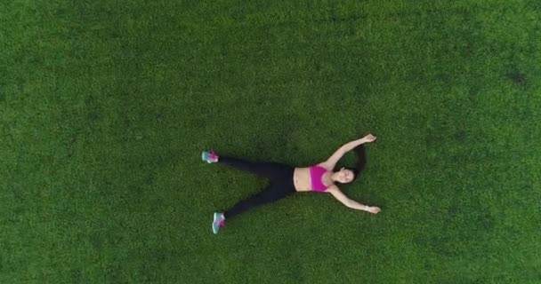 Luchtfoto. atleet rust na de opleiding liggen op het gazon in het stadion. jong meisje van bovenaf volgens sportkleding — Stockvideo