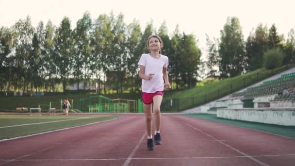 Una ragazzina che fa jogging allo stadio. il bambino va a fare sport all'aria aperta. sport per bambini . — Video Stock