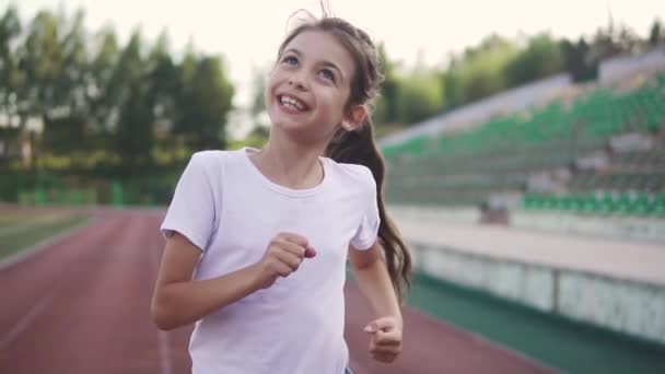 Liten flicka åtnjuter jogging. barnet kör längs spåret på stadion — Stockvideo