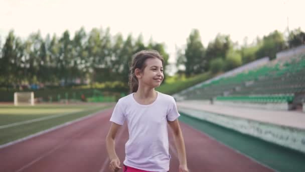 Portret dziewczynki cieszy, jogging. dziecko biegnie wzdłuż toru na stadionie — Wideo stockowe