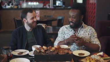 iki genç adam bir biftek bir restoranda yemek. iki arkadaş bir rahat restoranda bir masada oturmak ve eğlenceli konuşuyor