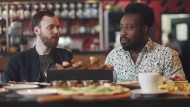 iki genç adam bir biftek bir restoranda yemek. iki arkadaş bir rahat restoranda bir masada oturmak ve eğlenceli konuşuyor