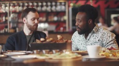 iki genç adam bir biftek bir restoranda yemek. iki arkadaş bir rahat restoranda bir masada oturmak ve eğlenceli konuşuyor. kolay yemek