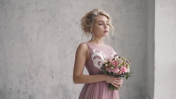 Portrait d'une jeune fille en robe de soirée. maquillage du soir et une belle coiffure. fille avec un bouquet de fleurs posant dans le studio — Video