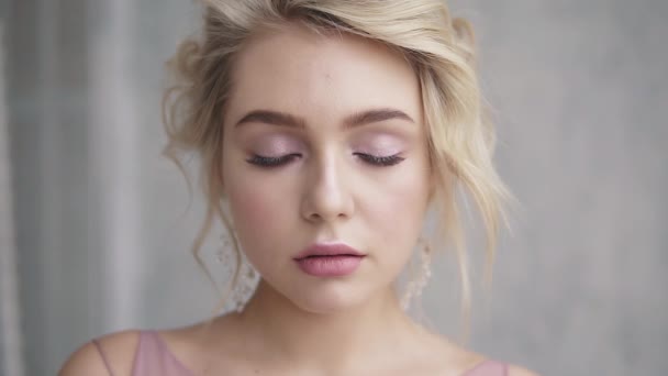 Retrato de cerca de una hermosa chica con ojos azules. rubia con hermoso maquillaje y peinado abre los ojos mirando y sonríe a la cámara — Vídeos de Stock