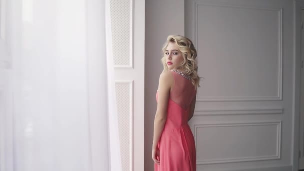 Портрет чарівної молодої блондинки в вечірній сукні. дівчина зі святковим макіяжем і волоссям посміхається і позує на камеру — стокове відео