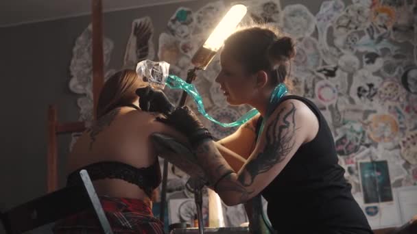 マスターのタトゥーは ホーム スタジオでタトゥーをやっています 女の子彫作業タトゥー マシンのホーム スタジオで 女の子が彼女の肩にタトゥー ストック動画 C Nskfoto