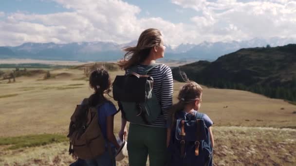 Família de turistas em uma viagem. mãe com duas filhas na campanha. crianças com mochilas admiram a vista das montanhas — Vídeo de Stock