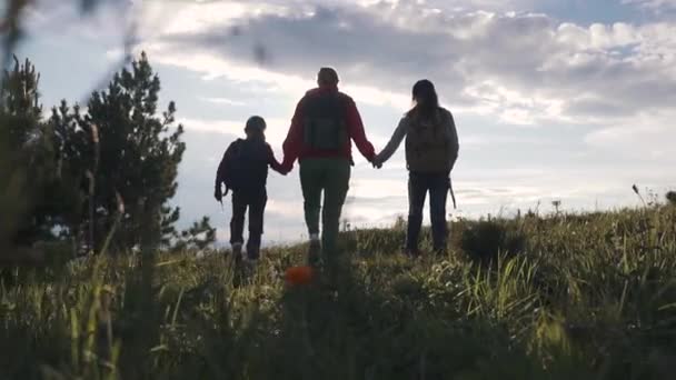 Οικογένεια των τουριστών σε ένα ταξίδι. μητέρα με δύο κόρες στην εκστρατεία. τα παιδιά με σακίδια, θαυμάστε τη θέα στα βουνά. νεαρή γυναίκα πηγαίνει με τα παιδιά στα βουνά. — Αρχείο Βίντεο