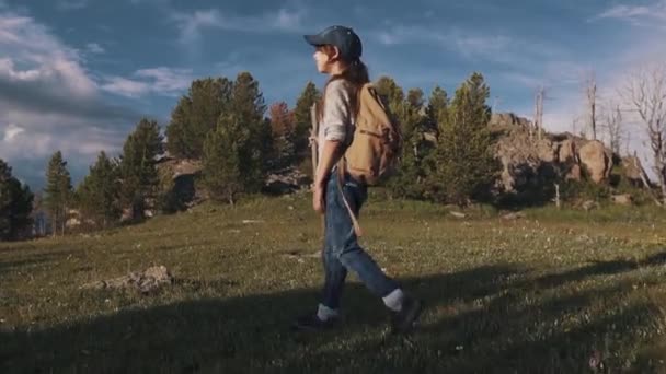 Pengembara gadis pergi Hiking di pegunungan. seorang anak kecil berada di jalur gunung. turis dengan ransel dan tongkat. gerak lambat — Stok Video