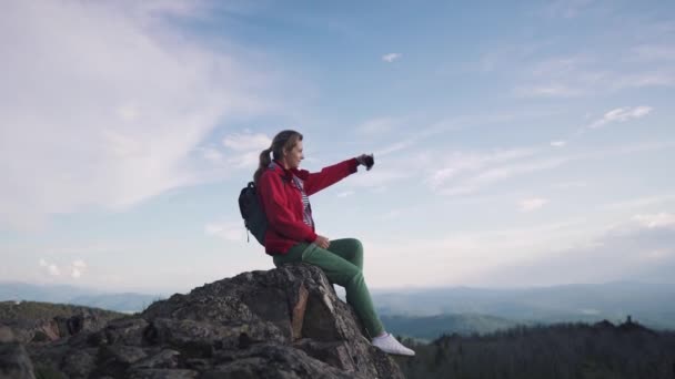 Il viaggiatore si fa un selfie in montagna. giovane turista donna seduta sul bordo di una scogliera e scattare foto sullo smartphone fotocamera — Video Stock