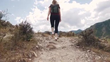 kız bir kayalık arazide bir yolda yürüyor. Genç kadın turist bir sırt çantası ile