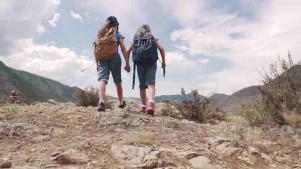 Niños viajeros con mochilas. el concepto de aventura y nuevos descubrimientos. dos niñas van contra el fondo de las montañas — Vídeo de stock