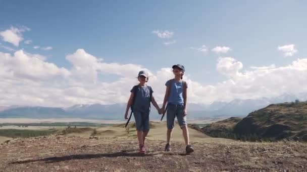Tourismus mit Kindern. Kinderreisende. zwei kleine Mädchen mit Rucksäcken gehen auf Wanderschaft und halten sich an den Händen. — Stockvideo