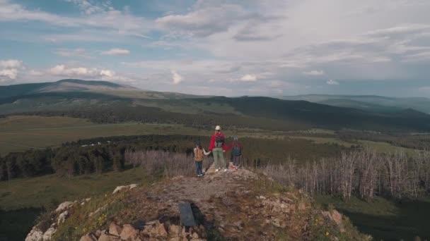 Aérea. familia de turistas. una joven con niños caminando por un sendero en las montañas. Una madre joven y niños con mochilas van de excursión. vista posterior — Vídeos de Stock