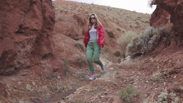 Chica turista en gafas de sol va en un terreno inusual. montañas rojas y tierra roja como en Marte . — Vídeos de Stock