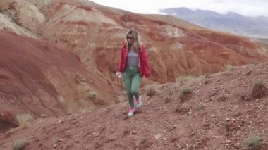 Güneş gözlüklü kız turist alışılmadık bir arazi üzerinde gider. Kırmızı dağlar ve kırmızı yeryüzünde Mars olarak.