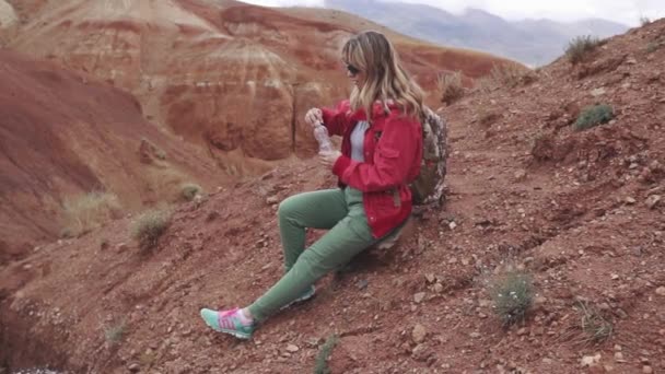 Turisten dricker vatten ur flaskan under resten. röda bergen och röda jorden som på Mars. — Stockvideo