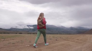 Uzun yürüyüşe çıkan kimse sert hava dağlık arazide yürür. bulutlar dağ zirveleri aşağıda. uzun bir yürüyüş üzerinde turist kızla. Arkadan görünüm