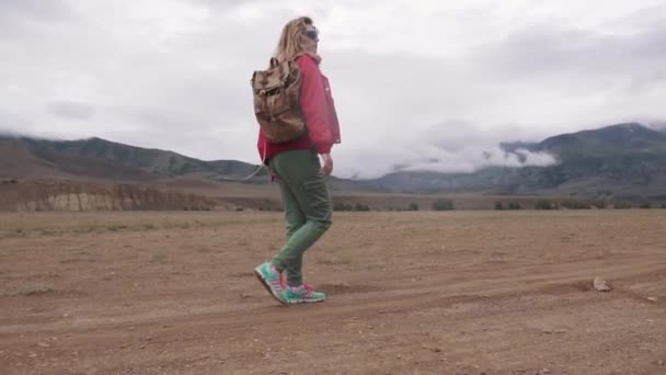 Escursionista cammina sul terreno montuoso con tempo inclemente. nuvole sotto le cime delle montagne. ragazza con un turista in escursione . — Video Stock