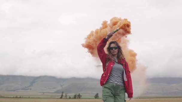 Pelancong perempuan dengan batang asap memberikan tanda dan menarik perhatian dengan asap berwarna. gadis wisatawan memegang granat asap berwarna. gerak lambat — Stok Video