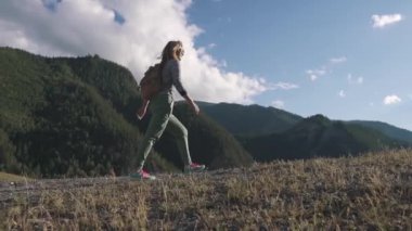 dağlar ve bulutlar arka planda kız gezgin. Bir turist bir sırt çantası ile yokuş yukarı yükselir.