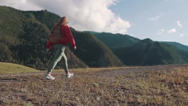 Путешественник взбирается на гору. девушка туристка с рюкзаком за плечами, идущая по горной местности — стоковое видео
