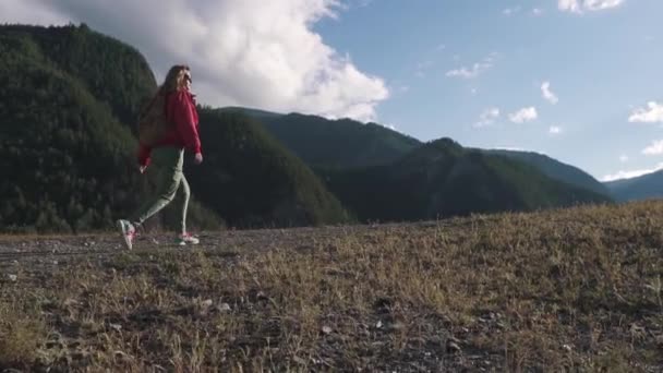 Porträtt av en turist med en ryggsäck bakom hans axlar i bergen. flicka resenär i solglasögon klättrar kullen — Stockvideo