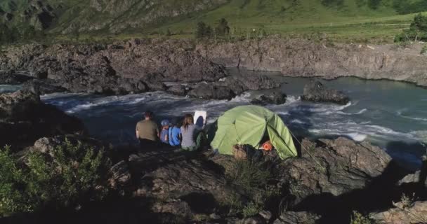 空中。一个有孩子的旅行者家庭坐在帐篷附近, 欣赏高山河和山脉的景色。. — 图库视频影像