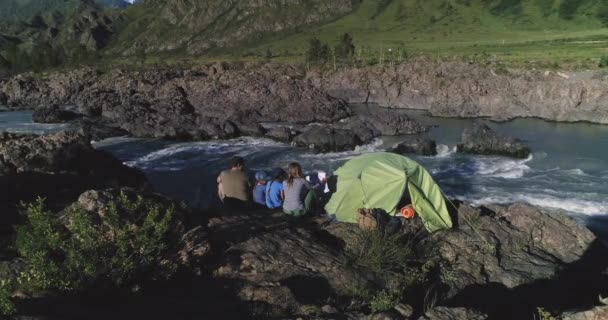 空中。一个有孩子的旅行者家庭坐在帐篷附近, 欣赏高山河和山脉的景色。. — 图库视频影像