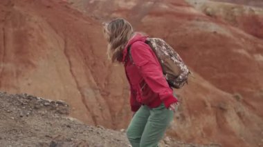 Gezgin dik bir yokuş yükselir. bir turist kız bir sırt çantası ve dağlık arazi yürüyüş giyen güneş gözlüğü.